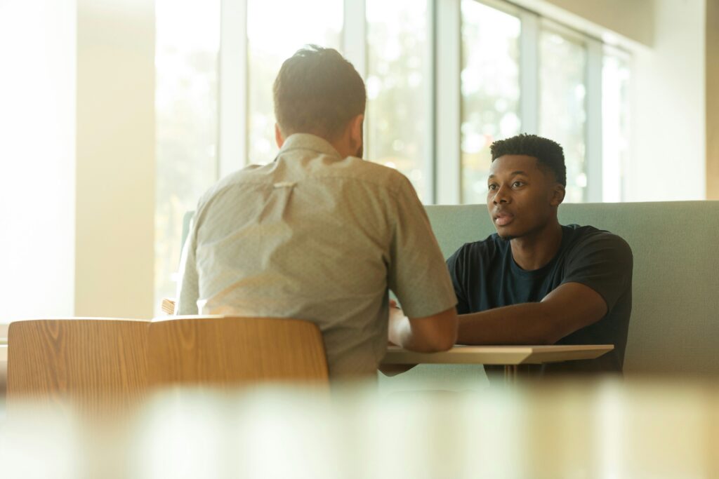A confident job candidate answering an interview question while speaking with a hiring manager in a professional office.